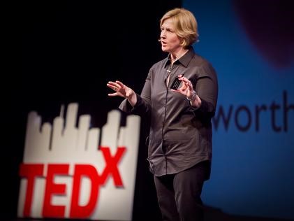 Image of woman speaking on a stage with blue background and TEDX logo